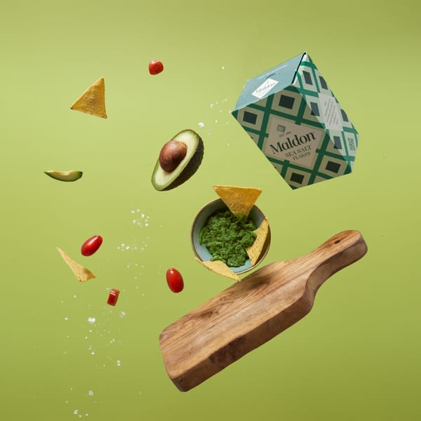 A wooden cutting board, a bowl of guacamole, and a series of ingredients floating in front of a green background