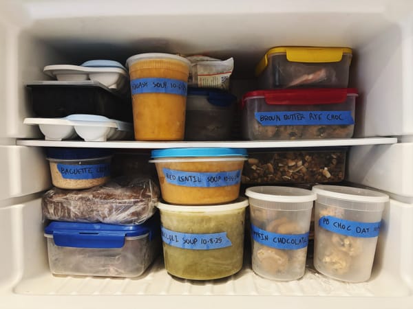 A freezer packed with plastic containers of soup and cookie dough
