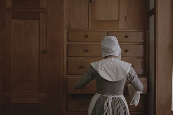 Photograph of a woman in a Shaker dress and bonnet opening a linen drawer